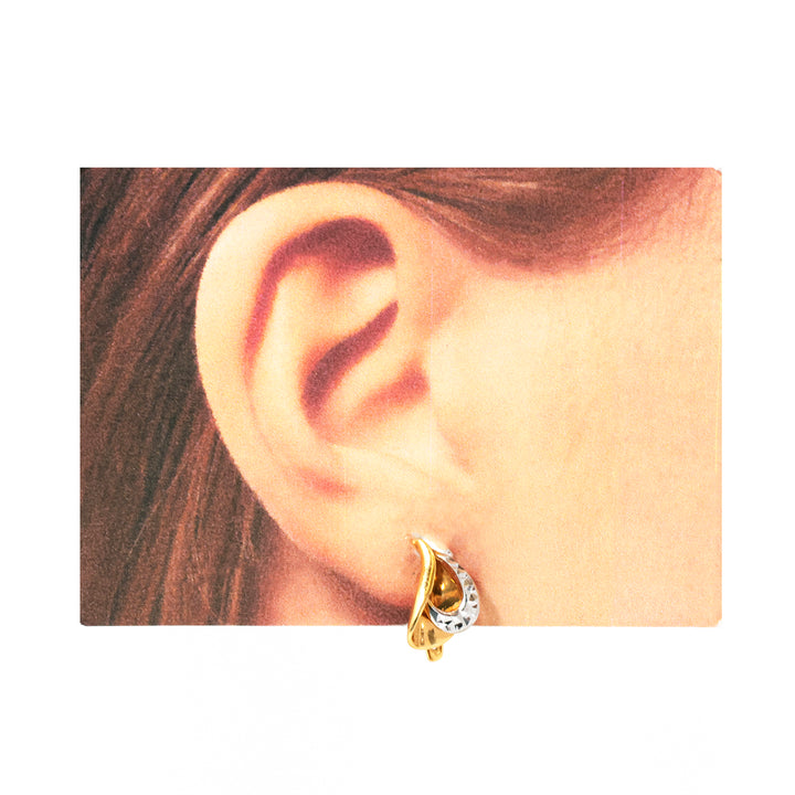 Gold earring worn on an ear with a plain background