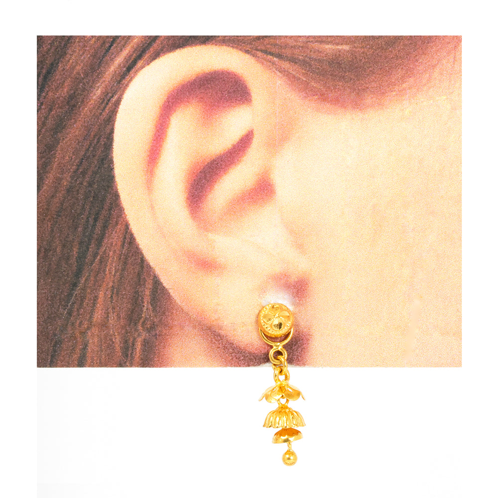 Gold earring worn on an ear with a plain background