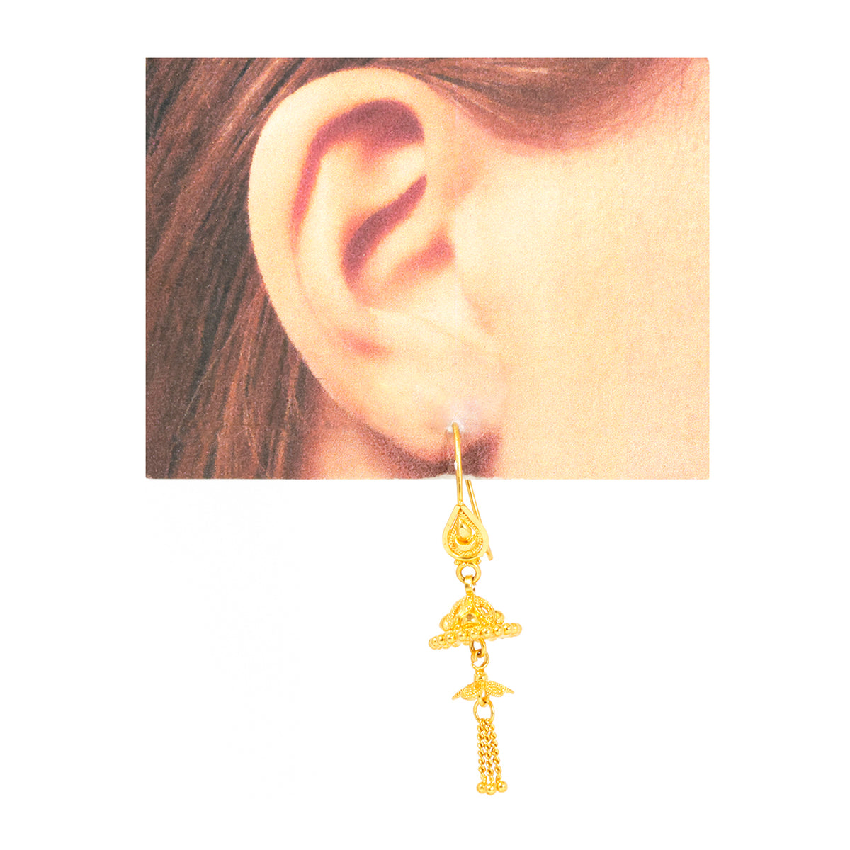 Gold earring worn on an ear with a plain background