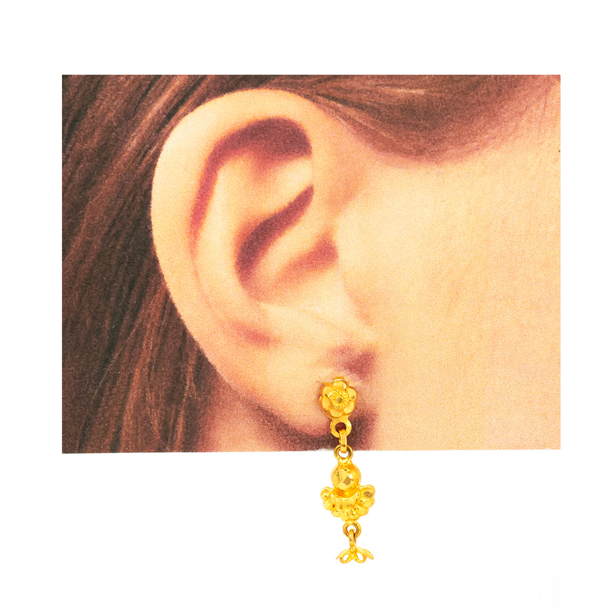 Gold earring worn on an ear with a plain background
