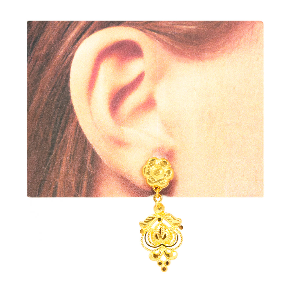 Gold earring worn on an ear with a plain background