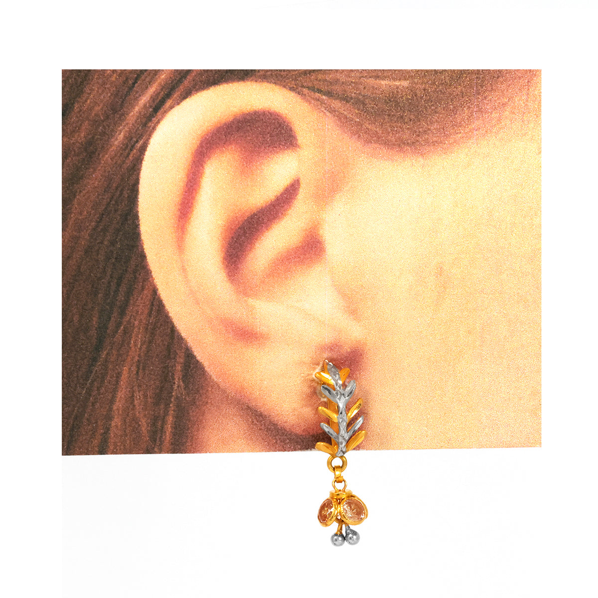 Gold and silver earring worn on an ear with a plain background