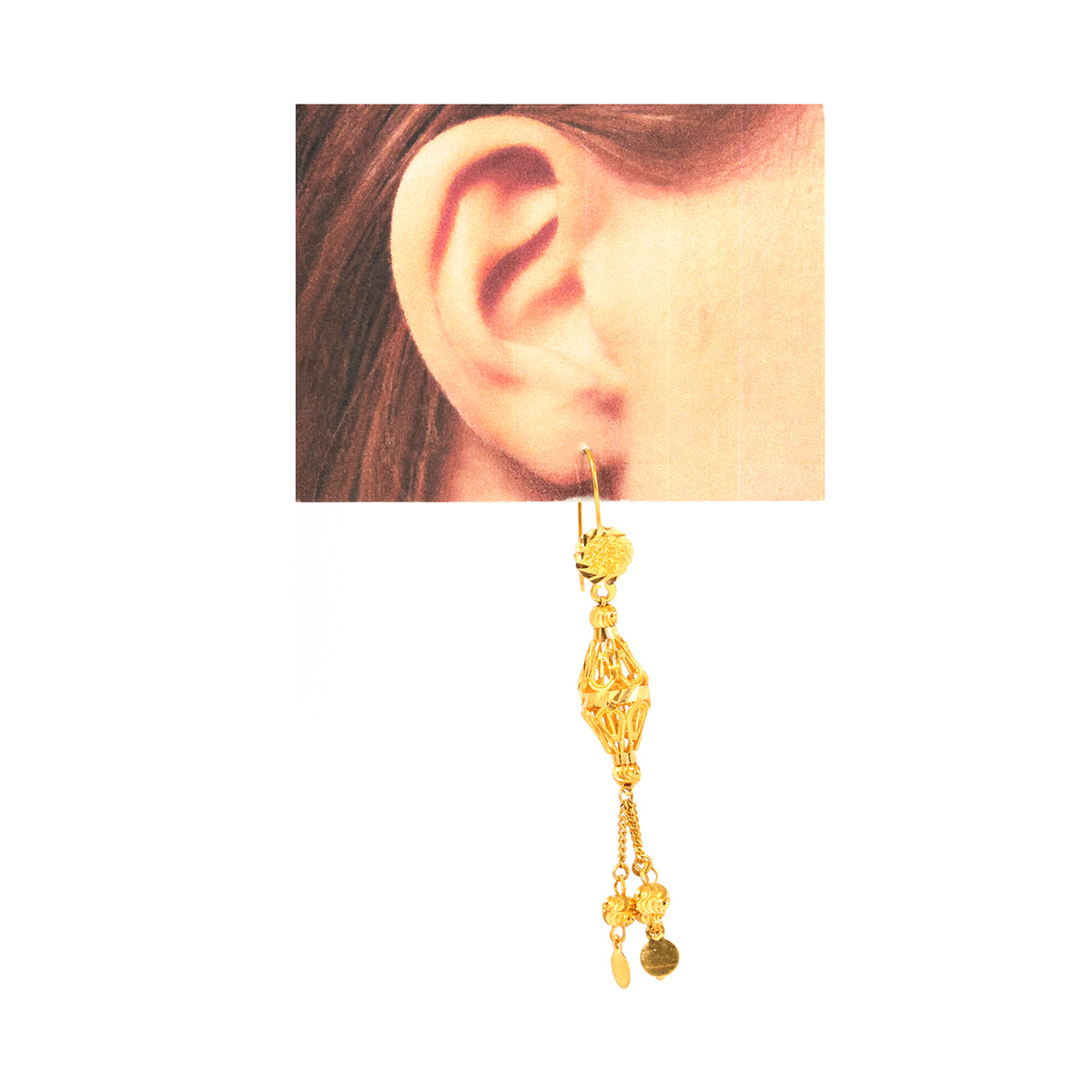 Gold earring worn on an ear with a plain background