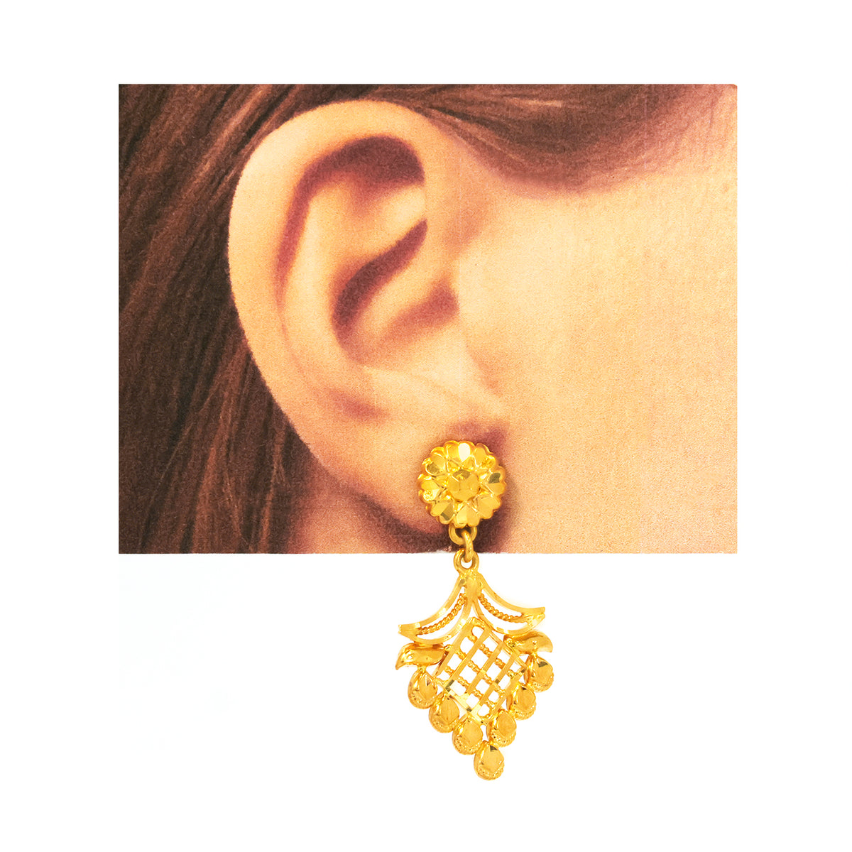 Gold earring worn on an ear with a plain background