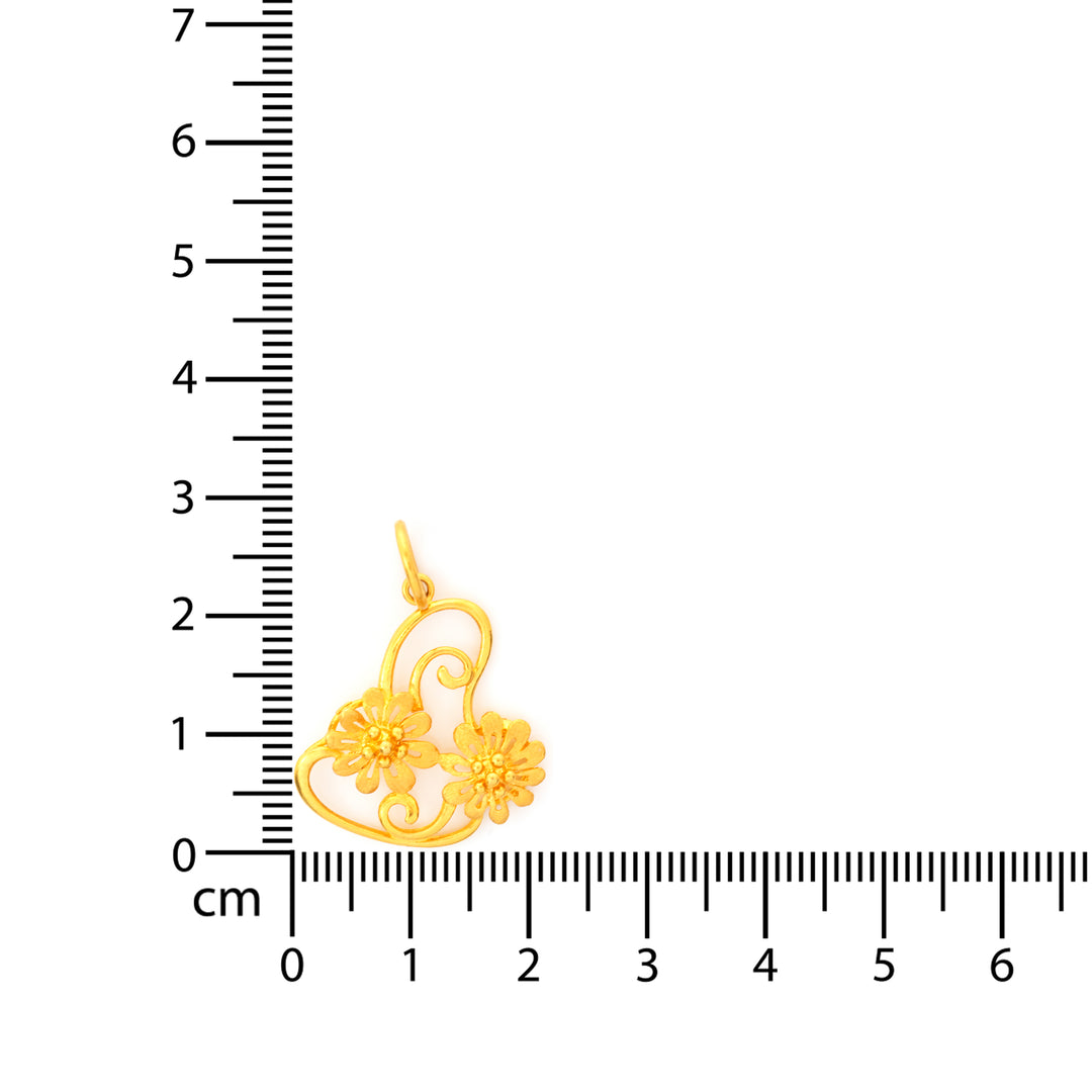 Gold pendant with floral design next to a ruler on a white background
