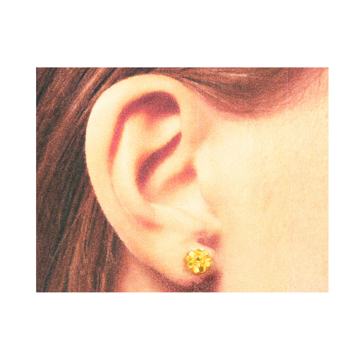 Close-up of an ear wearing a gold floral earring on a white background