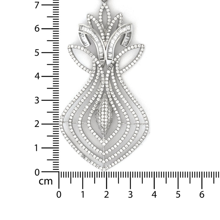 Decorative silver pendant with a ruler for scale on a white background