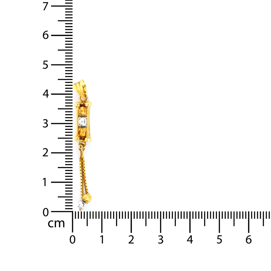 Gold pendant with a diamond measurement against a ruler on a white background