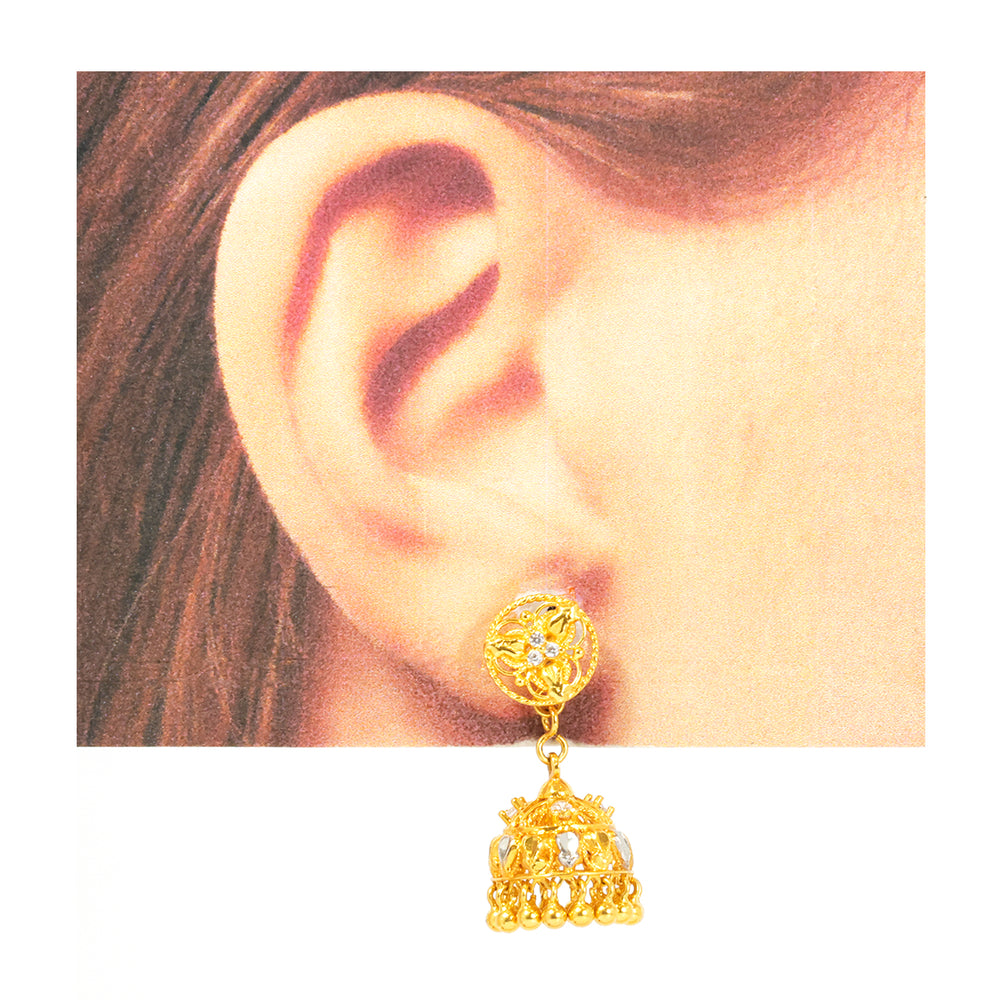 Gold earring worn on an ear with a plain background