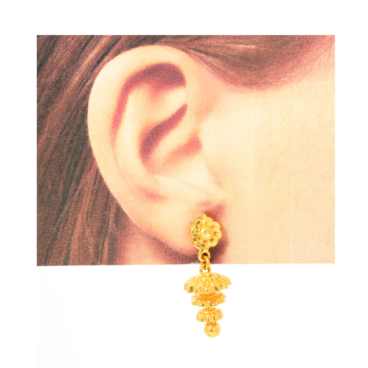 Gold earring worn on an ear with a plain background