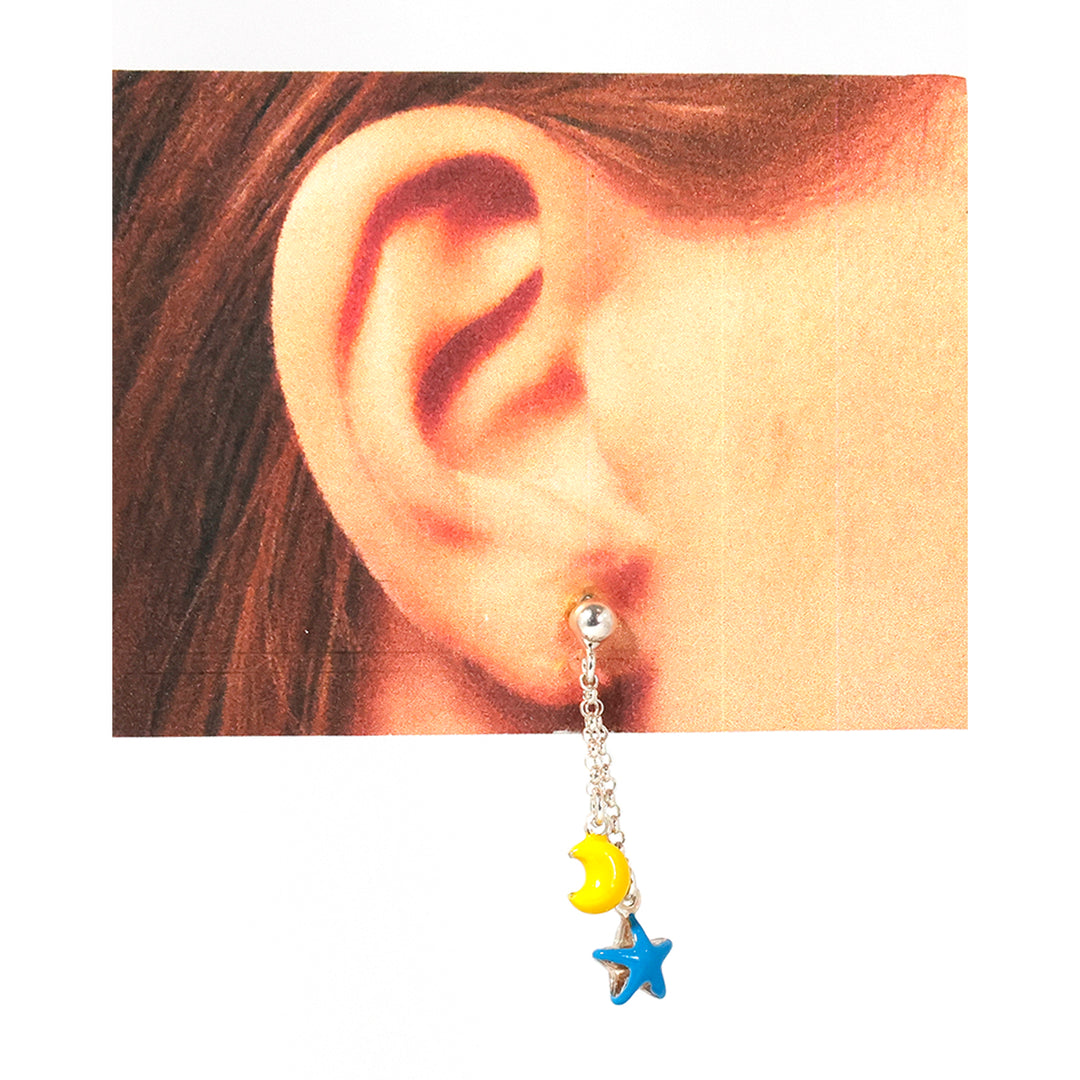 Close-up of an ear wearing a silver earring with yellow moon and blue star charms.