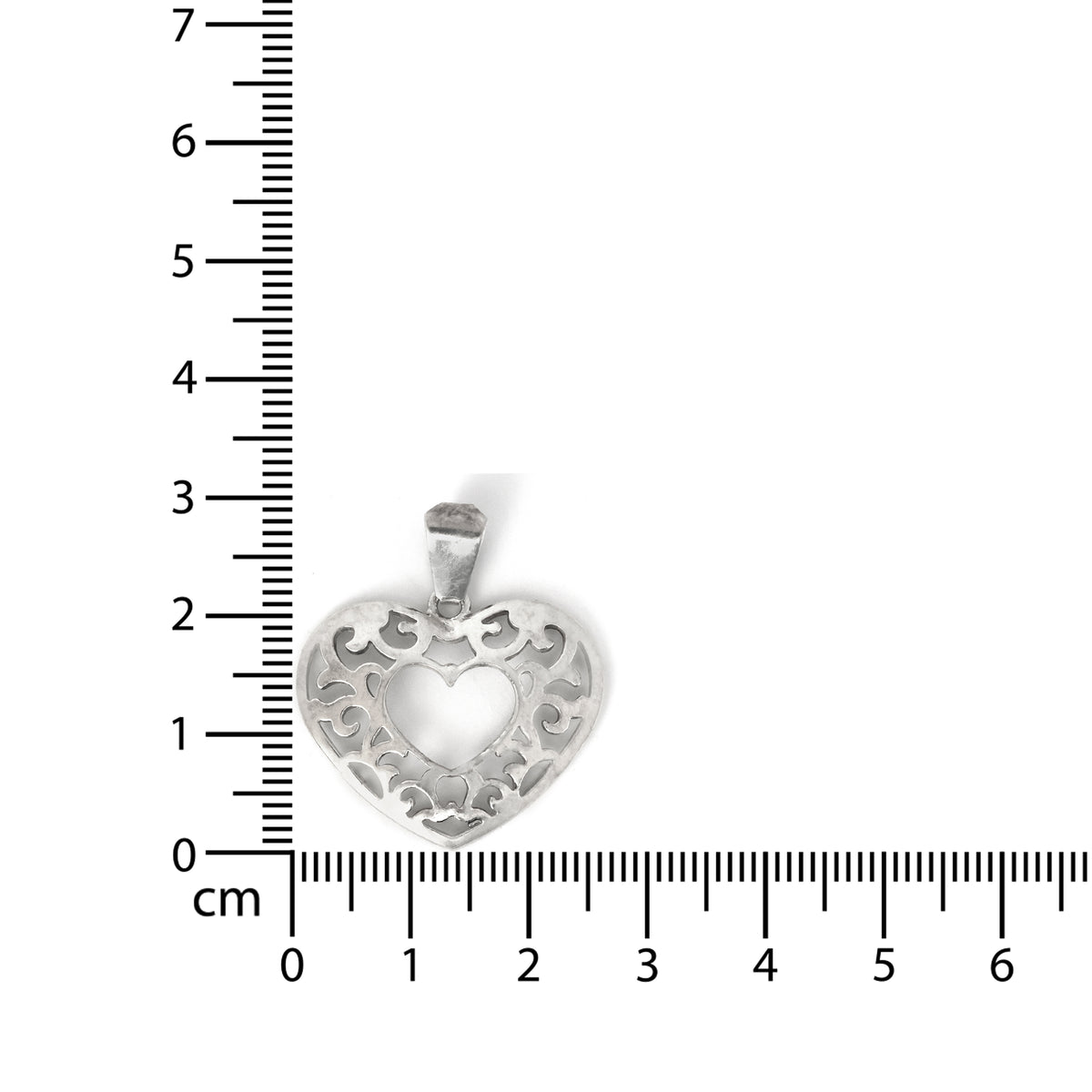 Silver heart-shaped pendant with intricate designs on a white background with a ruler for scale.
